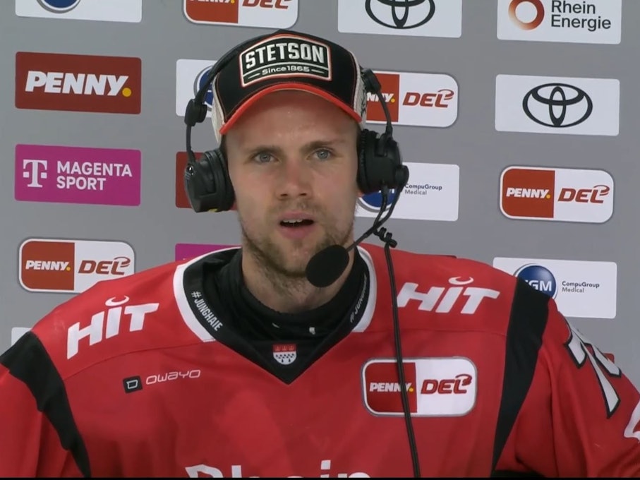 Dominik Bokk spricht mir Headset vor einer Sponsorenwand.