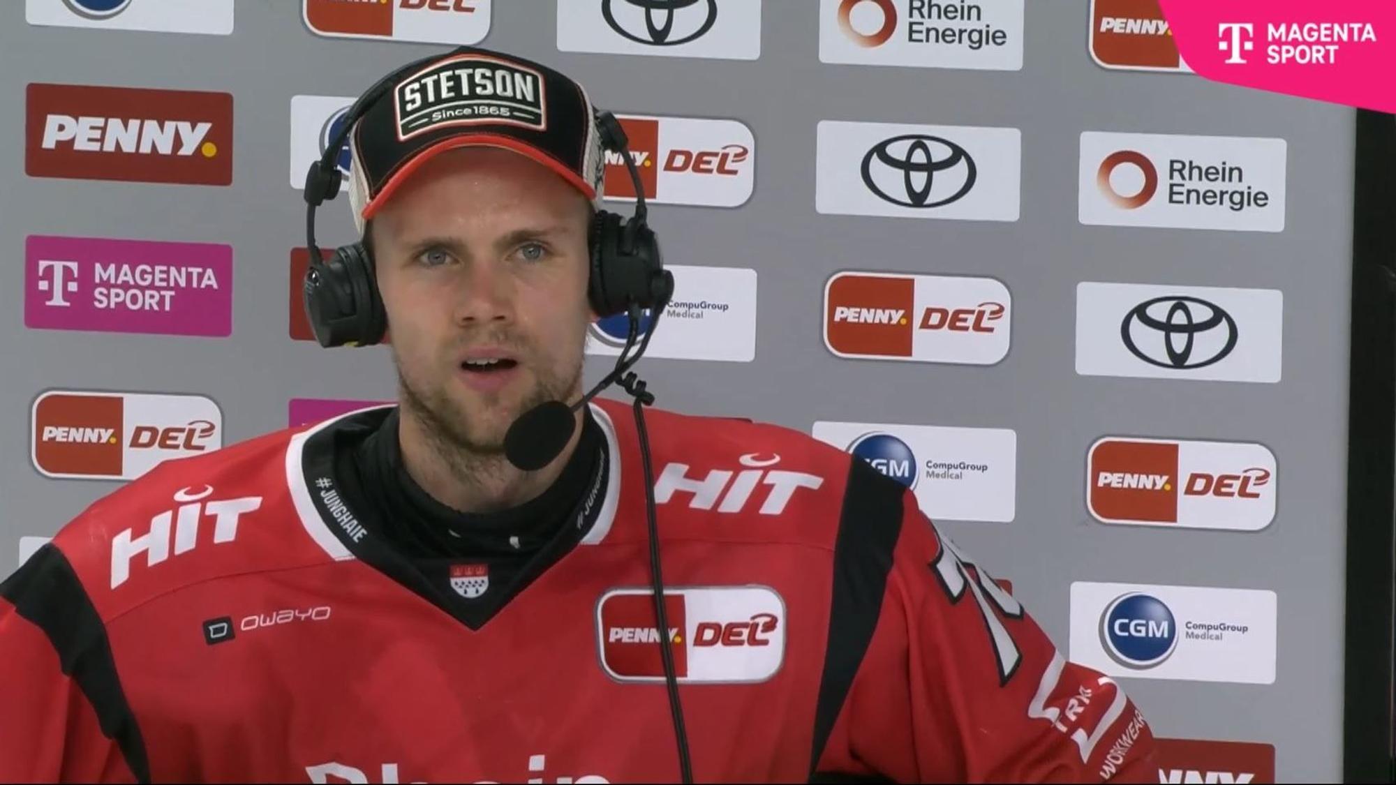 Dominik Bokk spricht mir Headset vor einer Sponsorenwand.