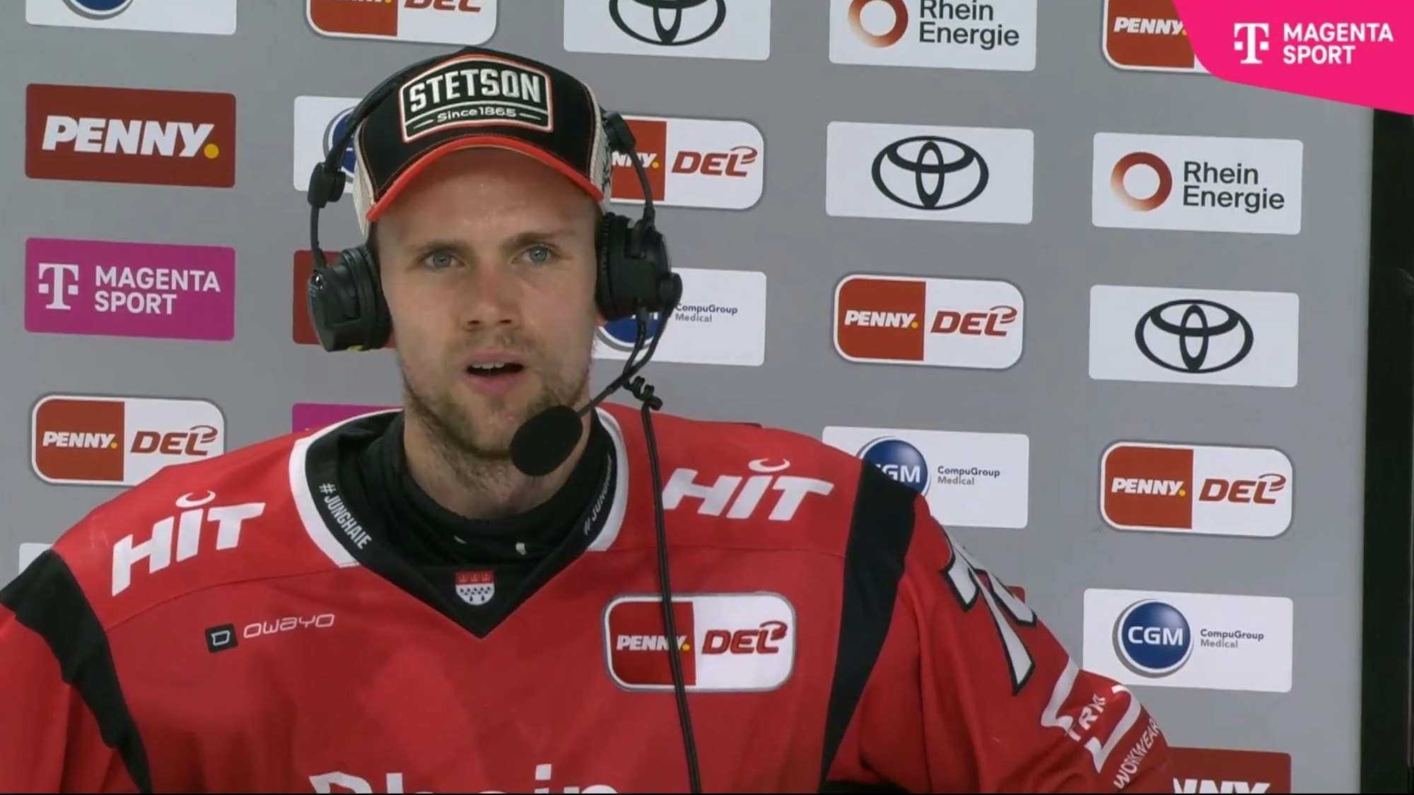 Dominik Bokk spricht mir Headset vor einer Sponsorenwand.