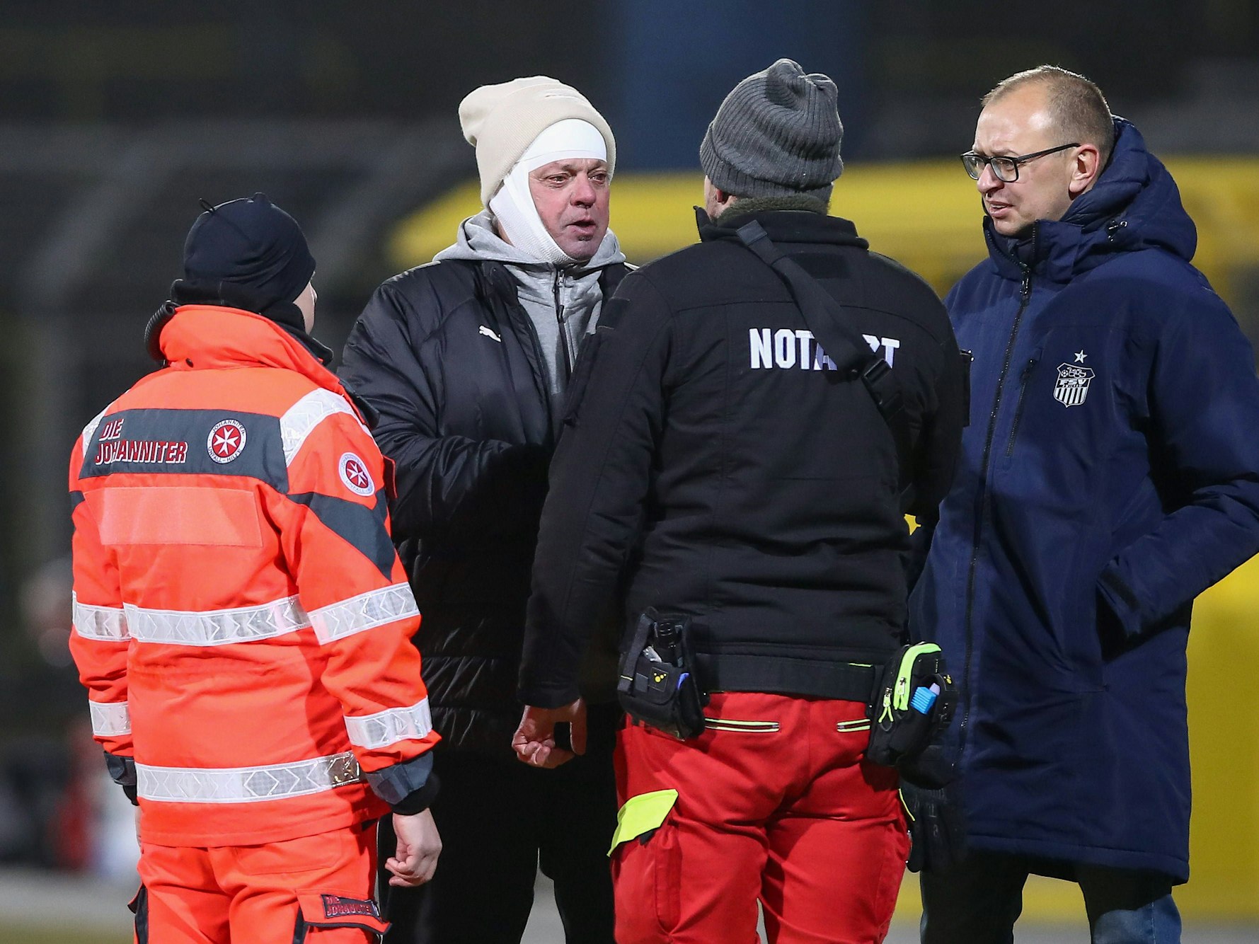Busfahrer Stephan Mildner spricht mit einem Notarzt, trägt einen Kopfverband unter der Mütze.