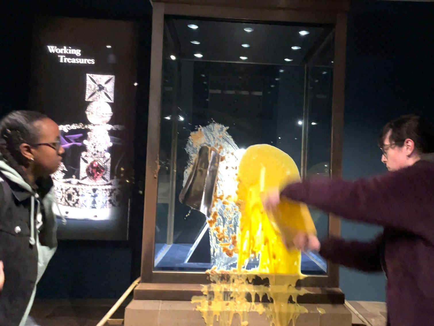 Handout aus einem von Take Back Power herausgegebenen Video, das zwei Unterstützerinnen von Take Back Power zeigt, die einen Nachtisch, mutmaßlich Apfel-Crumble und Vanillesoße, über die Kronjuwelen im Tower of London werfen. Der Tower of London ist nach dem Anschlag auf die Kronjuwelen bis auf weiteres geschlossen worden. Vier Menschen seien festgenommen worden, teilte die Polizei mit.