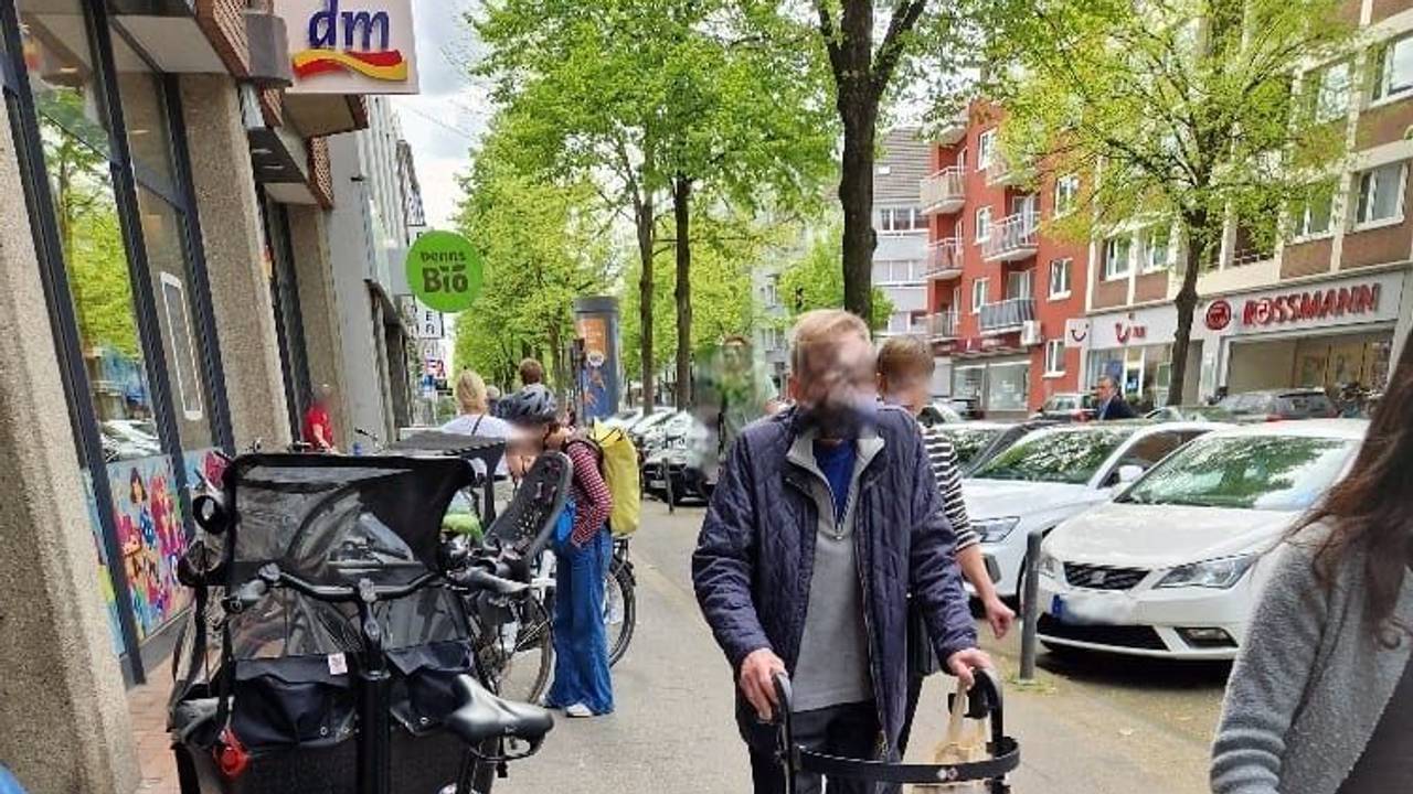 Ein Mann mit Rollator ist auf dem Gehweg unterwegs und muss an einem geparkten Lastenrad, das den halben Weg blockiert, vorbei.