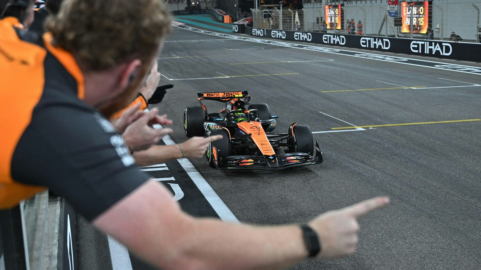 Lando Norris fährt über die Ziellinie, sein Team jubelt ihm zu.