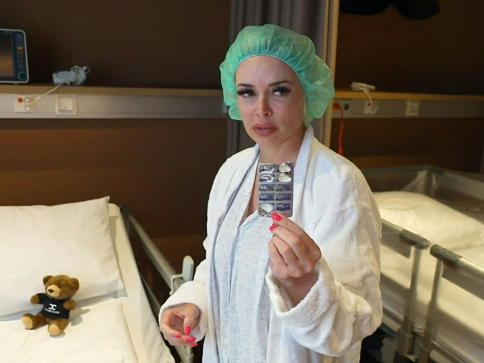 Daniela Katzenberger trägt eine OP-Haube und hält eine Packung Tabletten in die Kamera.