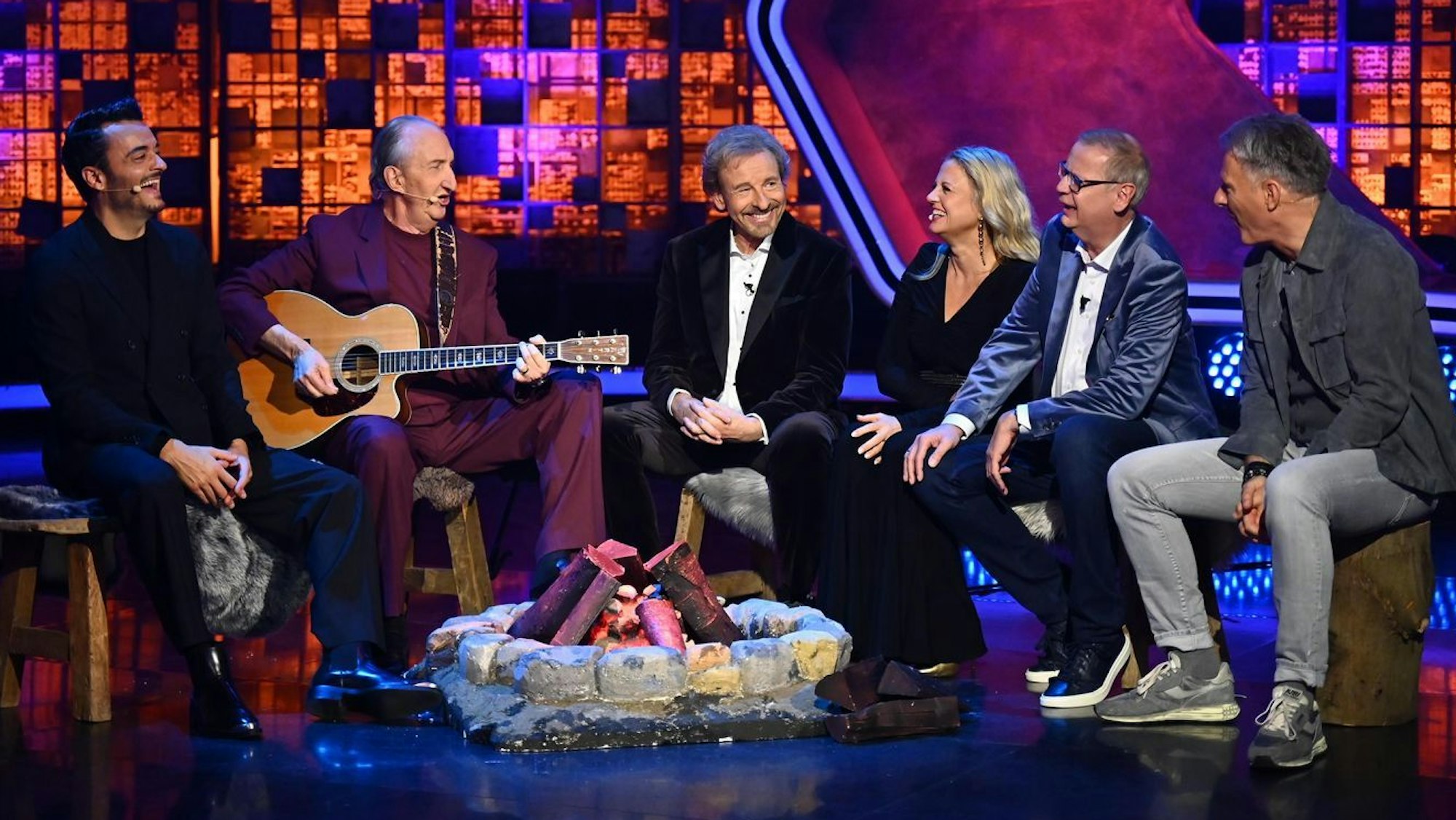Mehrere Menschen sitzen um Thomas Gottschalk auf einem Sofa, Mike Krüger hat eine Gitarre.