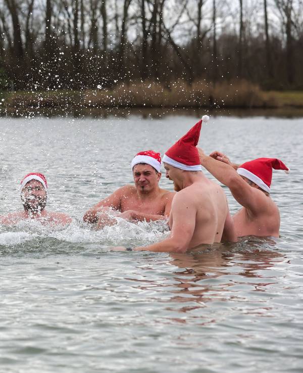 Männer und eine Frau mit Nikolausmützen baden in einem See.