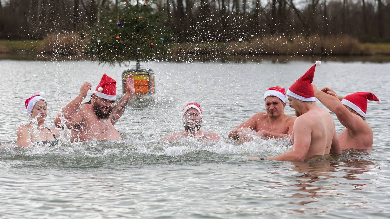 Männer und eine Frau mit Nikolausmützen baden in einem See.