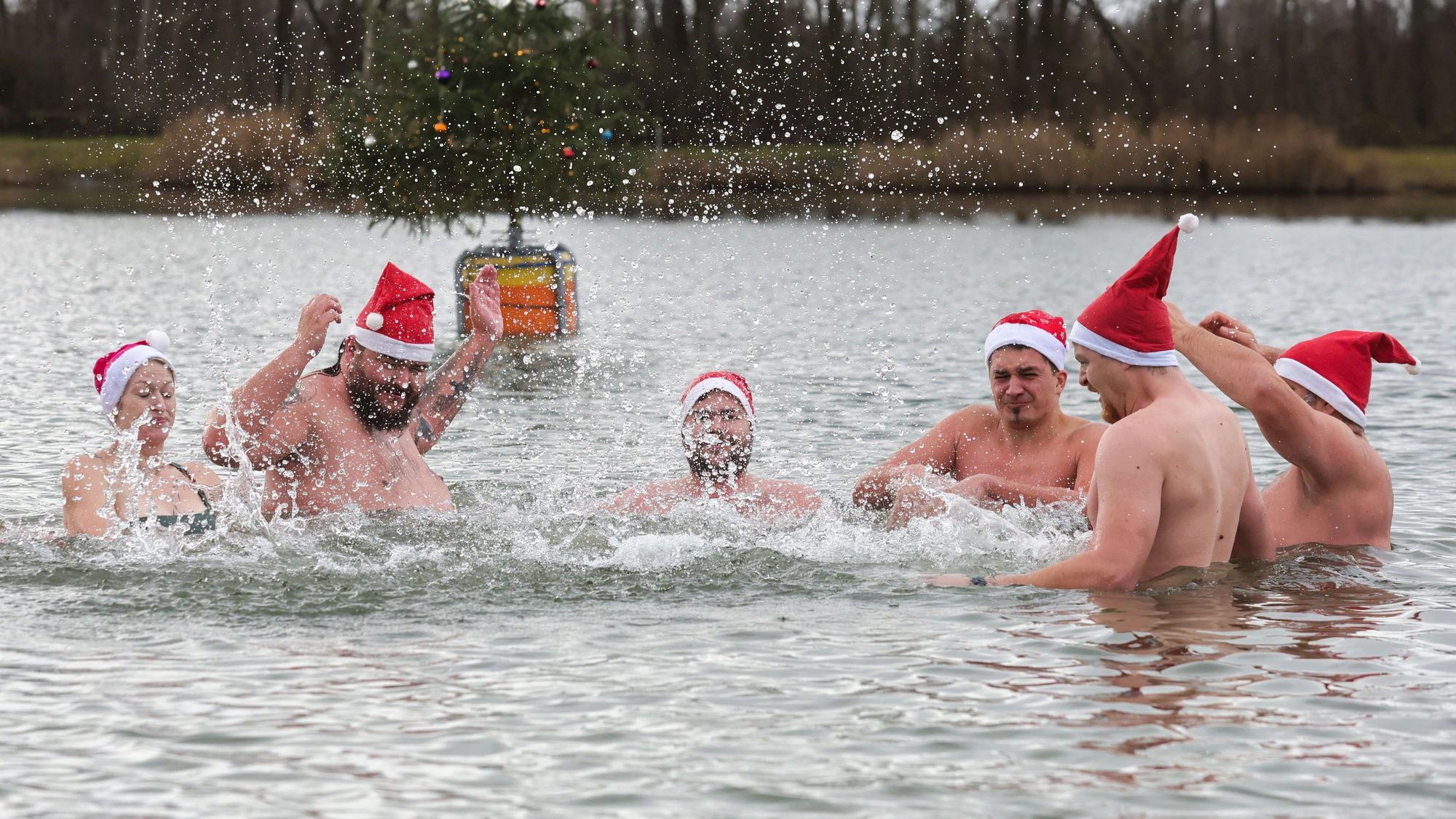 Männer und eine Frau mit Nikolausmützen baden in einem See.