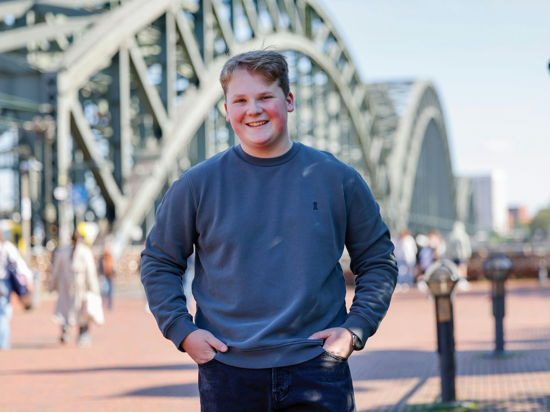 Julius Weckauf steht mit Händen in den Hosentaschen vor einer Brücke.