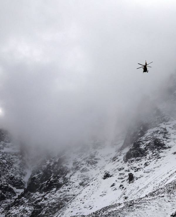 Ein Hubschrauber fliegt vor einem mit Schnee bedeckten Gebirge.
