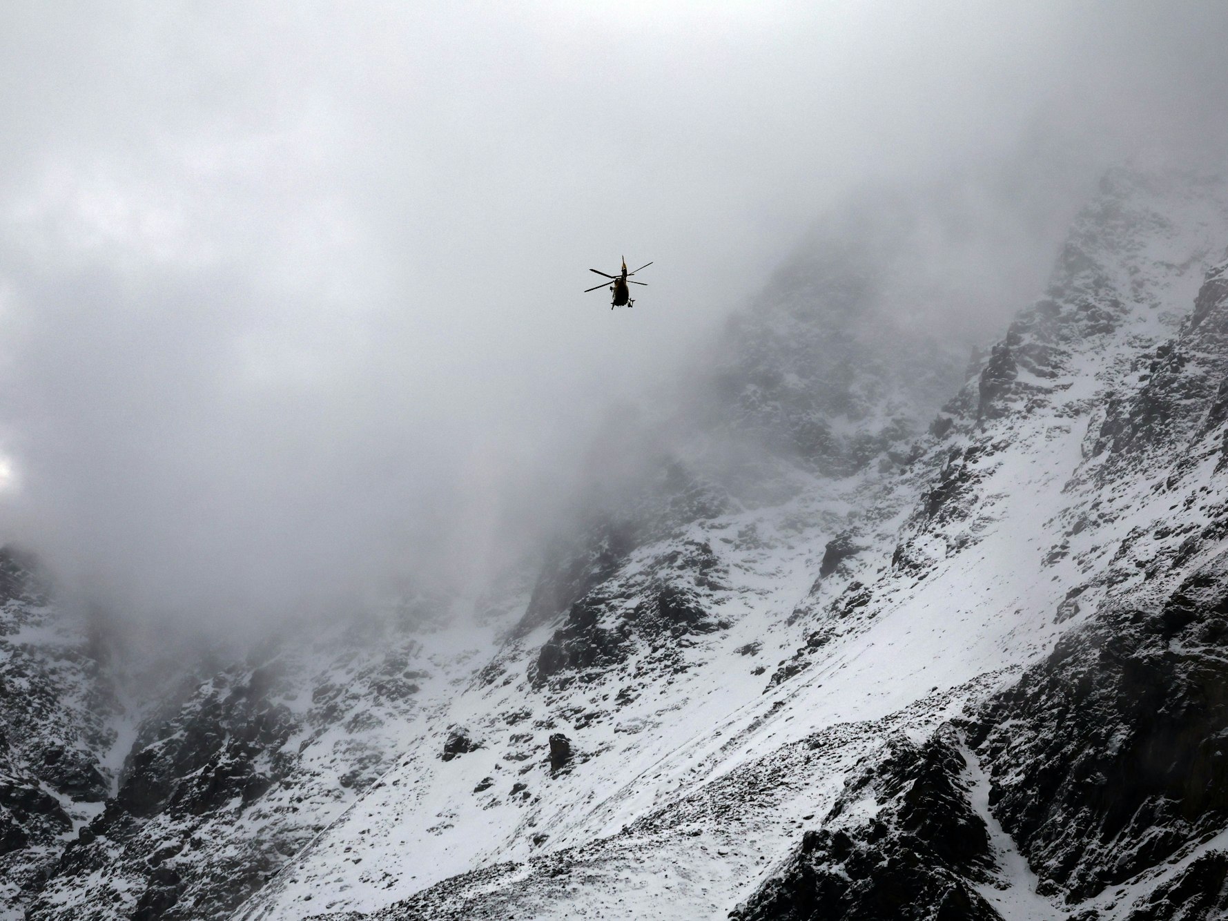 Ein Hubschrauber fliegt vor einem mit Schnee bedeckten Gebirge.