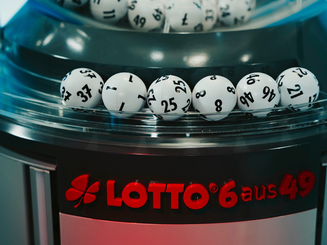Das Bild zeigt die gezogenen Lottozahlen-Kugeln in einer modernen Ziehungsmaschine. Im Vordergrund ist das rote Logo „LOTTO 6 aus 49“ zu sehen.