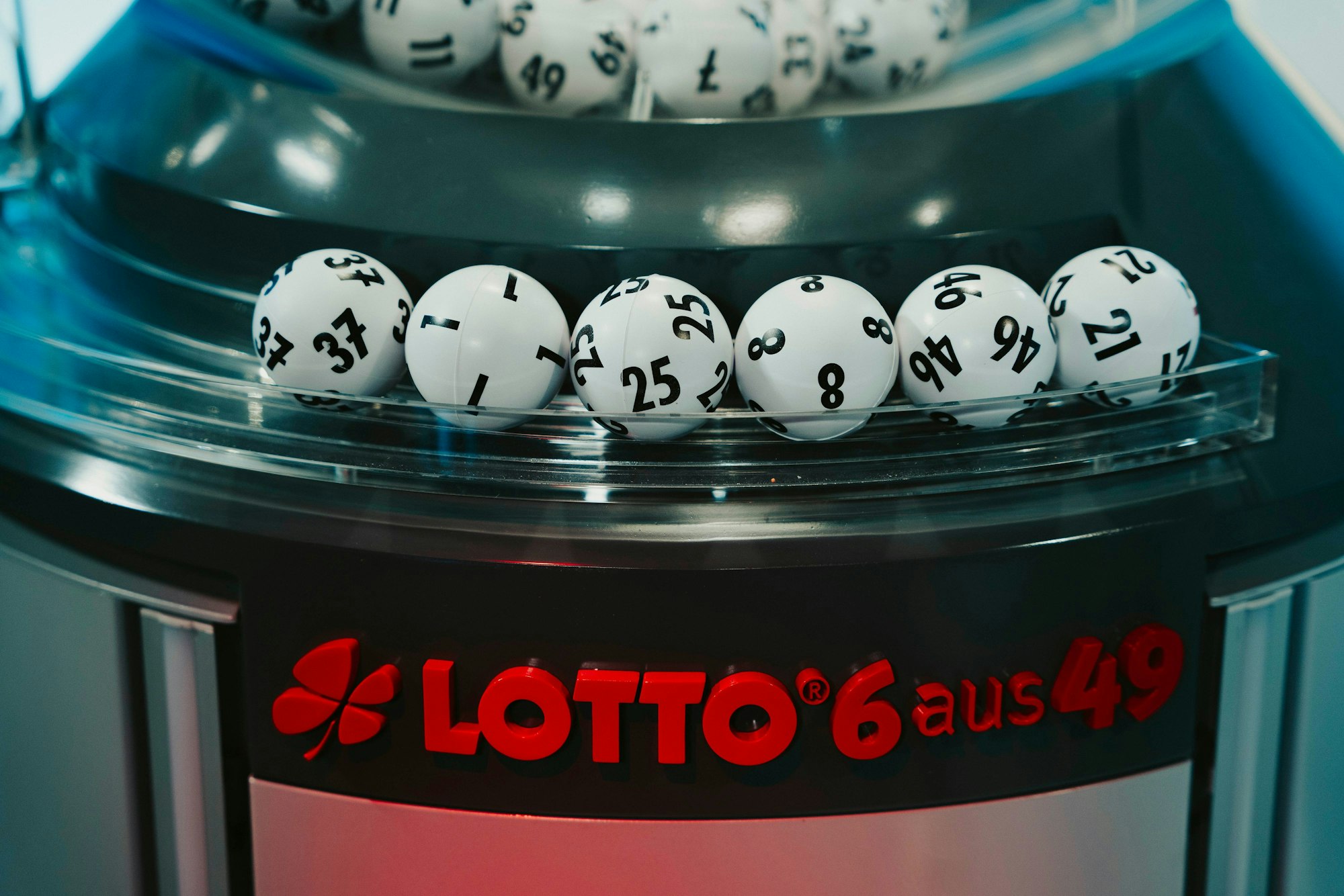Das Bild zeigt die gezogenen Lottozahlen-Kugeln in einer modernen Ziehungsmaschine. Im Vordergrund ist das rote Logo „LOTTO 6 aus 49“ zu sehen.