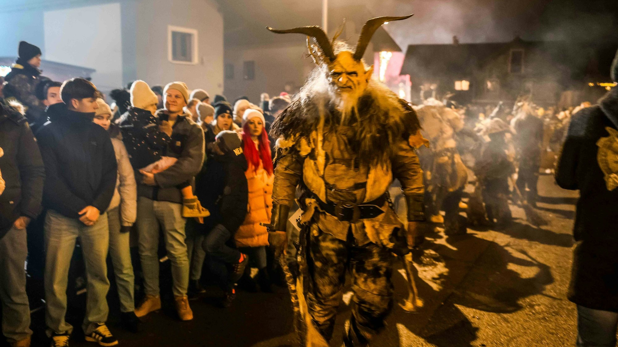 Ein gehörnter Krampus in traditionellem Kostüm inmitten einer Menschenmenge beim Perchtenlauf