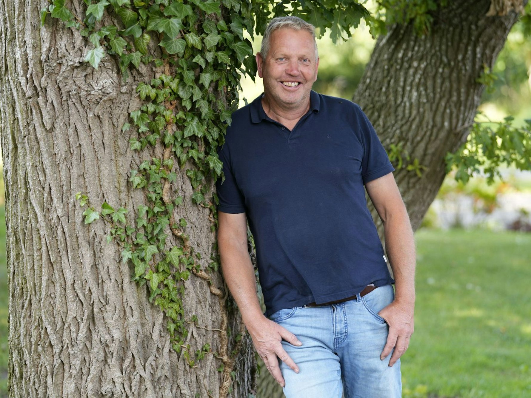 Ein Mann lehnt sich an einen dicken Baumstamm.