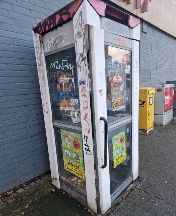 Eine Telefonzelle ist komplett beschmiert und mit Werbezetteln beklebt.