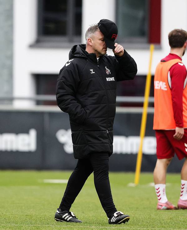 Lukas Kwasniok hält sich auf dem Trainingsplatz des 1. FC Köln eine Kappe vors Gesicht.