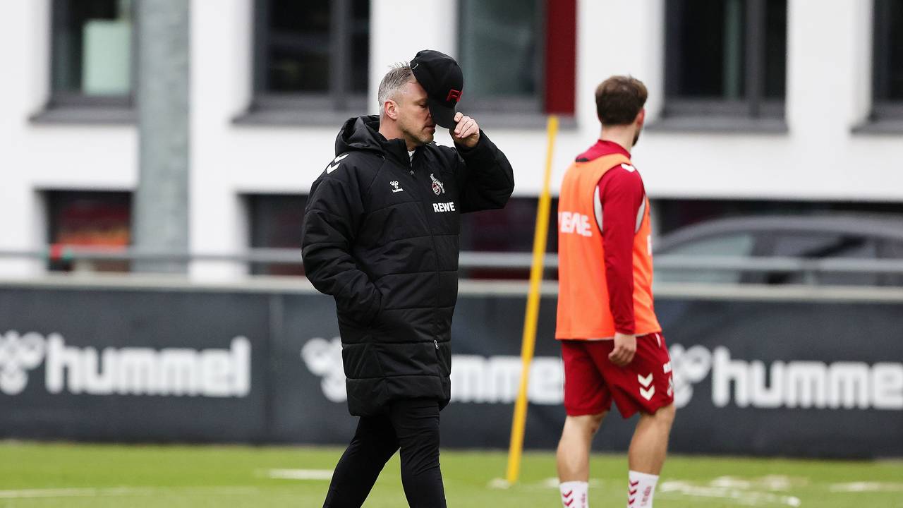 Lukas Kwasniok hält sich auf dem Trainingsplatz des 1. FC Köln eine Kappe vors Gesicht.