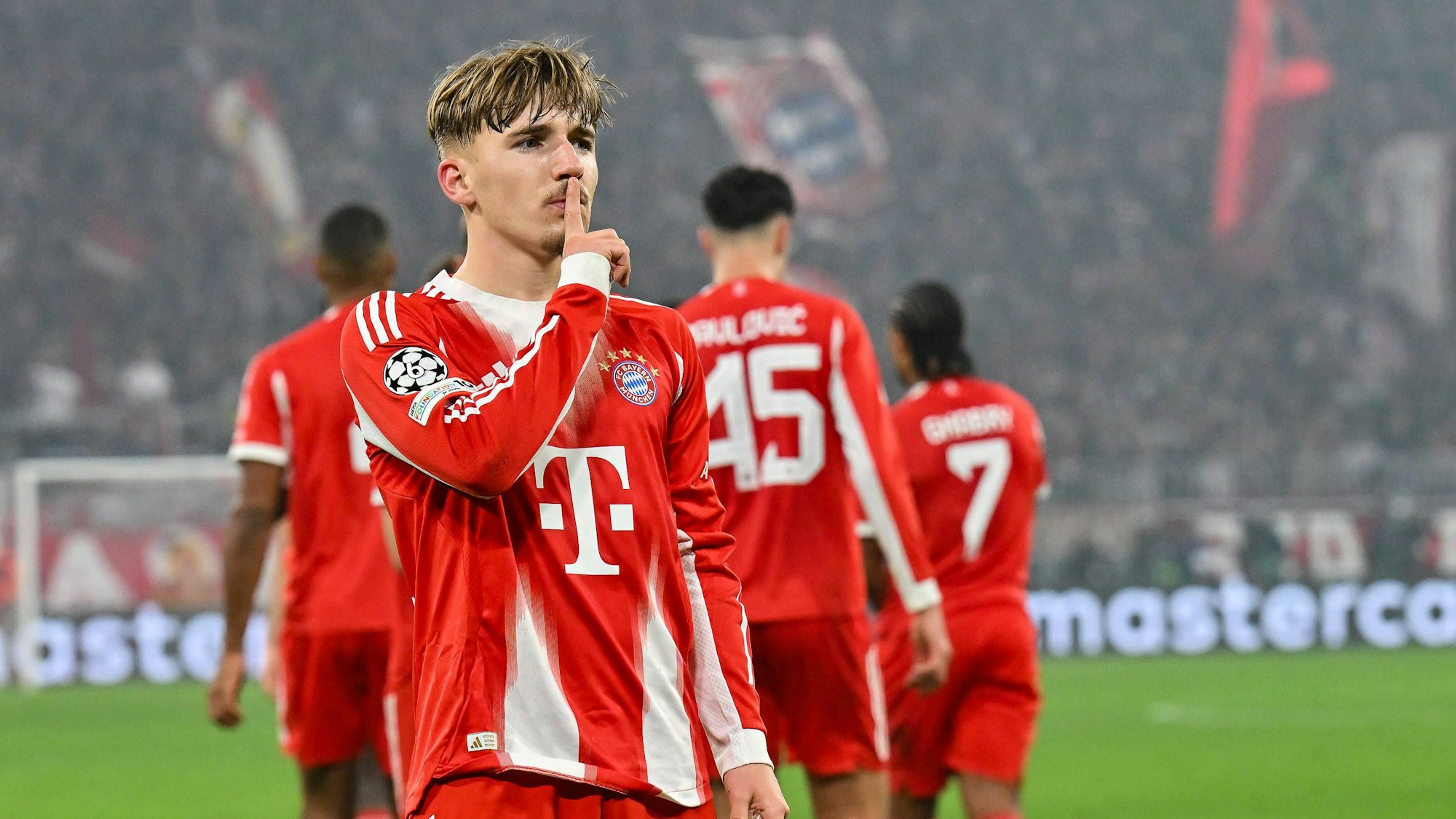 Lennart Karl hält sich bei einem Spiel des FC Bayern den Zeigefinger vor den Mund.