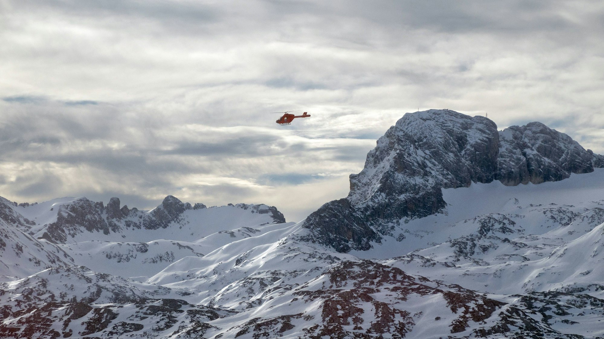 Rettungshubschrauber über schneebedeckter Berglandschaft mit Wolken