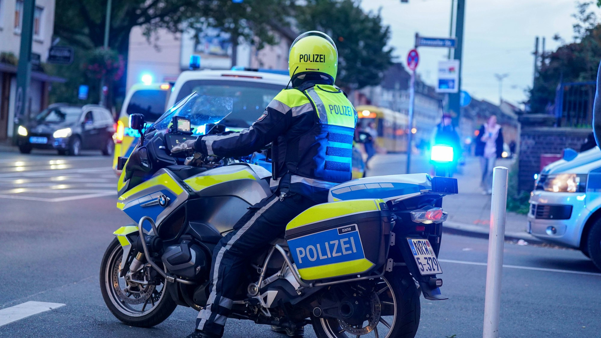 Symbolisches Bild eines Polizeimotorrads mit Beamtem und Blaulicht im Straßenverkehr.