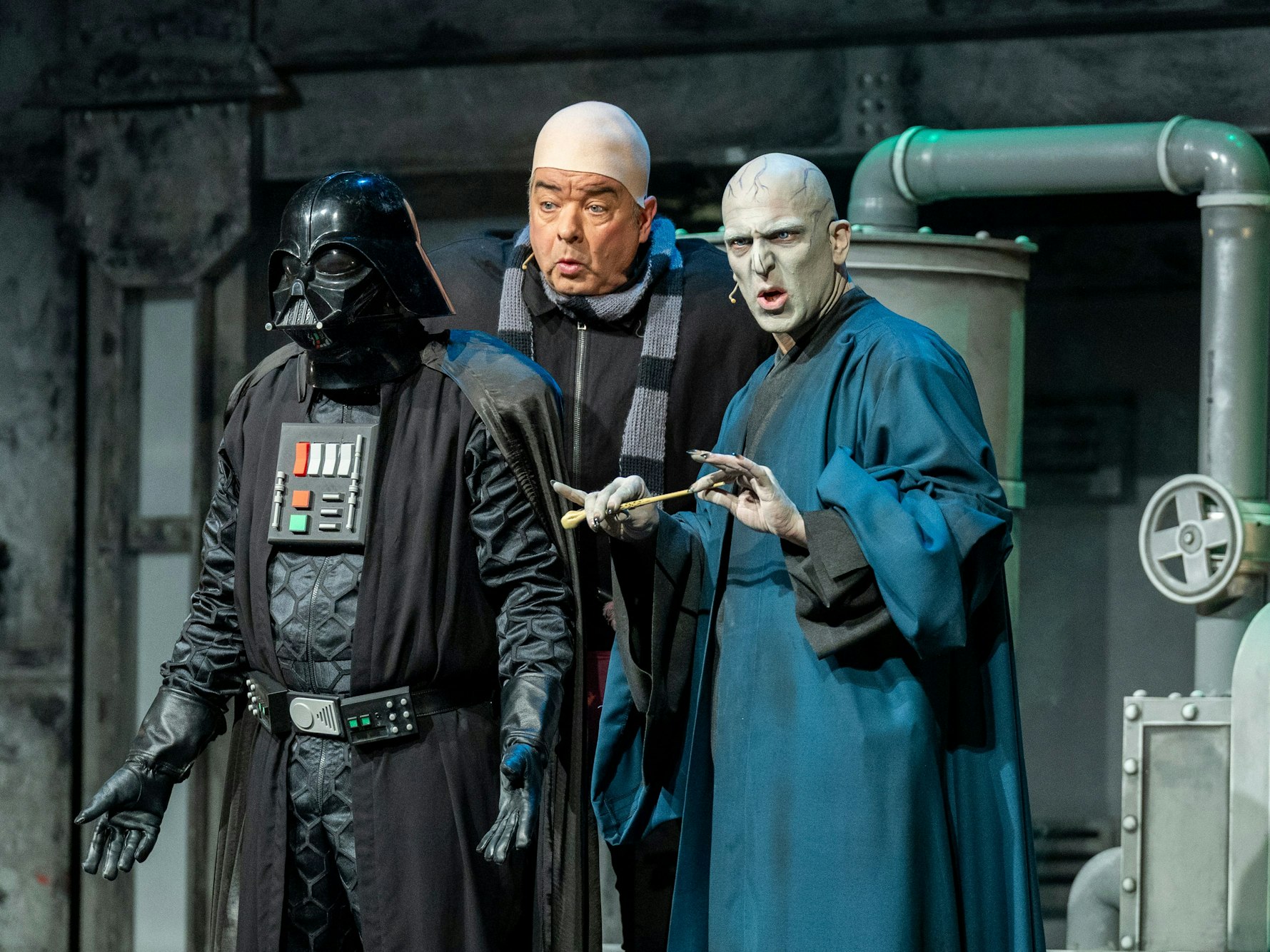 Drei verkleidete Personen stehen auf der Bühne, einer trägt einen Umgang und einen Helm.