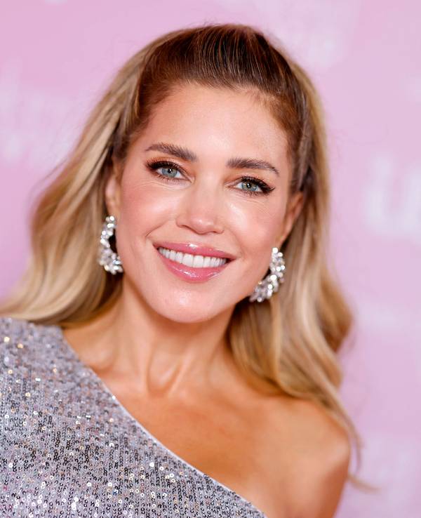 Sylvie Meis lächelt in funkelndem Oberteil vor rosa Hintergrund.