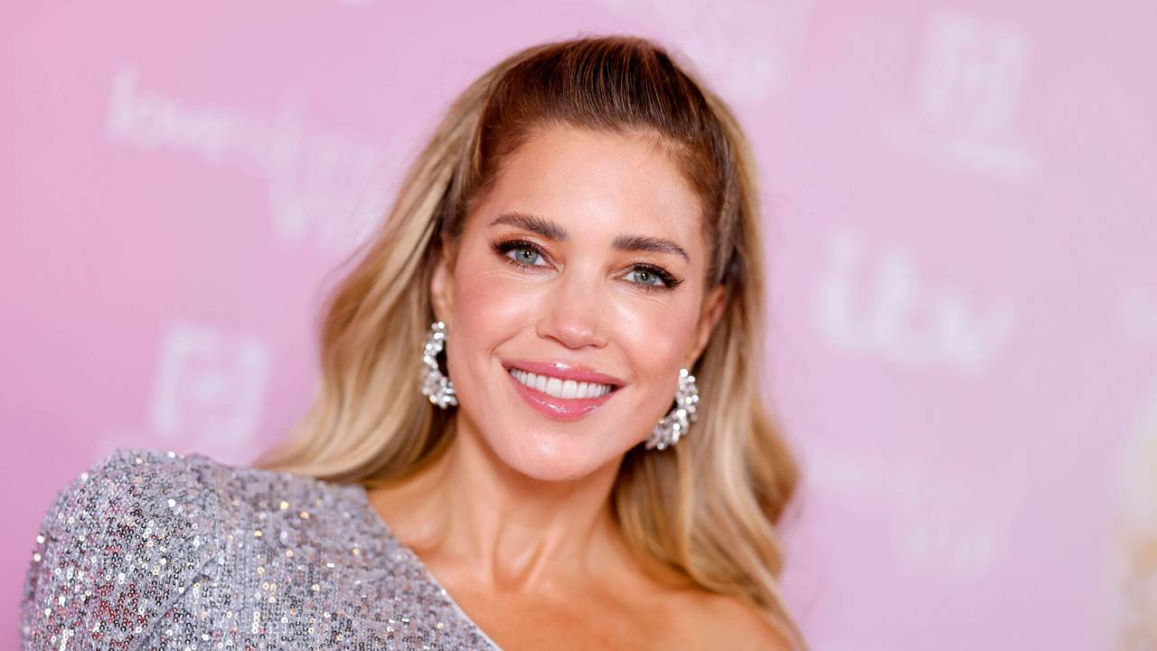 Sylvie Meis lächelt in funkelndem Oberteil vor rosa Hintergrund.