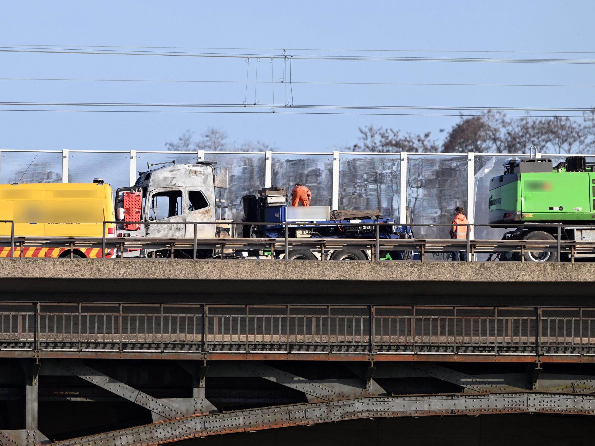 Auf einer Brücke steht ein ausgebrannter Lkw.