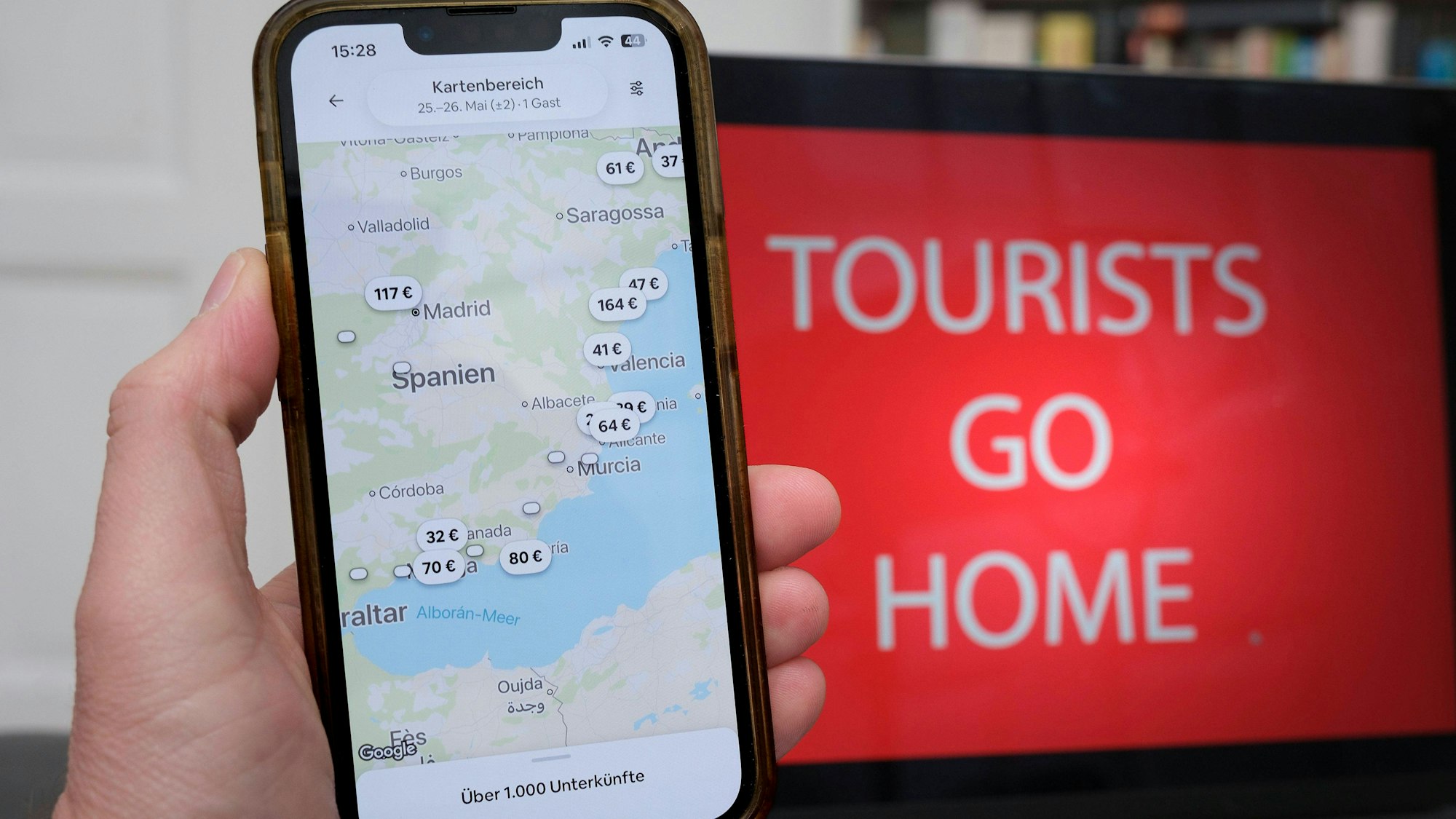 Smartphone mit Unterkünften, Laptop zeigt 'Tourists Go Home'-Botschaft