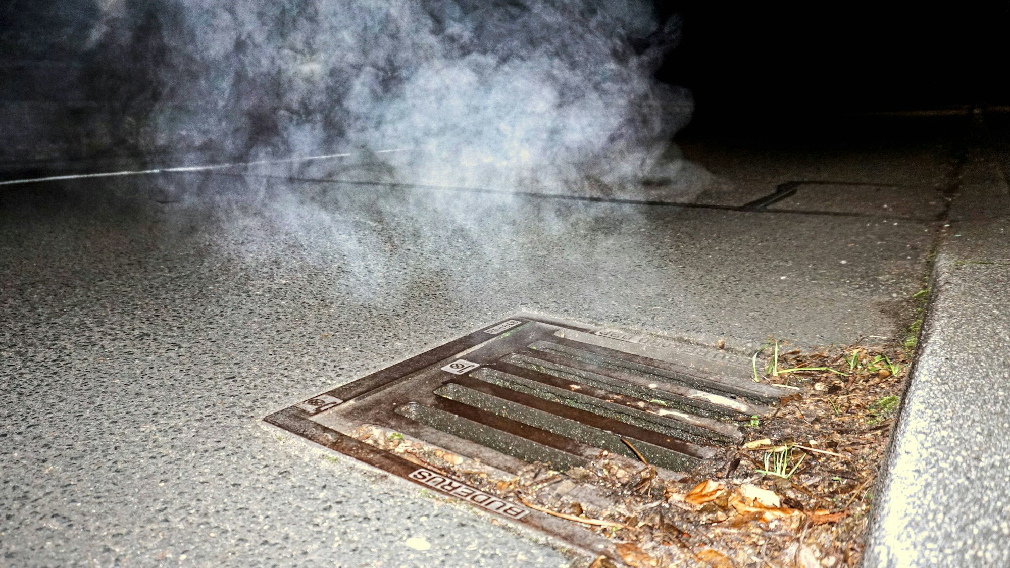 Kanalgas steigt bei Frost in der Dunkelheit aus einem Gulli