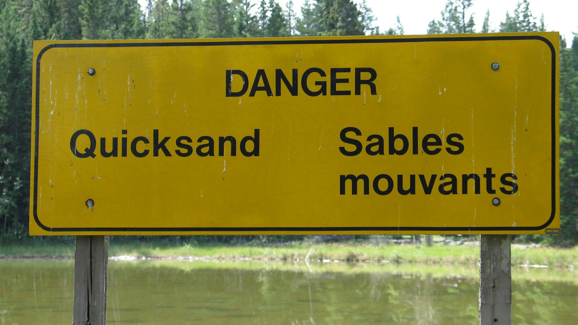 Gelbes Schild mit Aufschrift DANGER Quicksand Sables mouvants