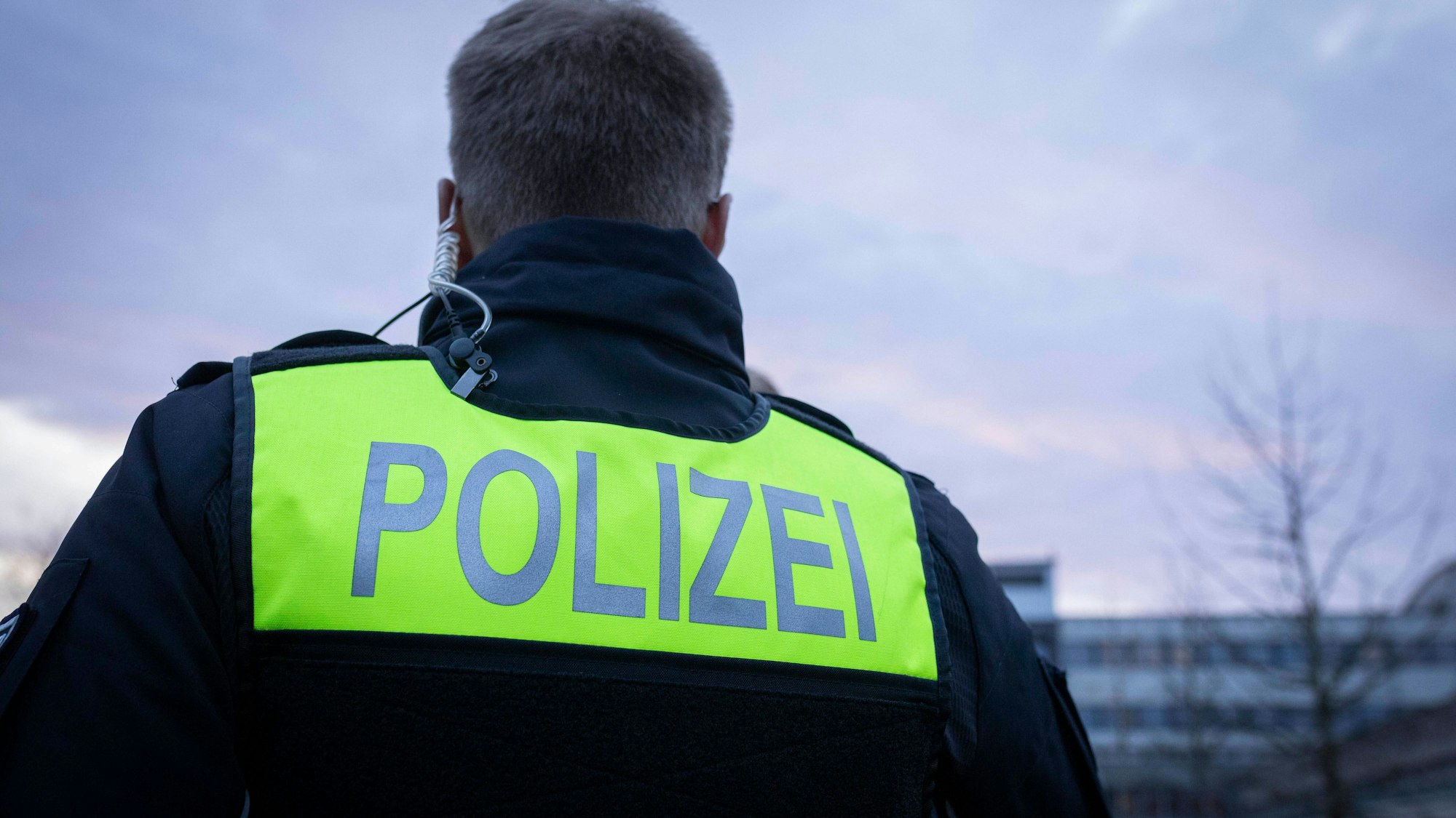 Rückenansicht Einsatzkraft mit gelbem POLIZEI-Schild und Schallschlauch