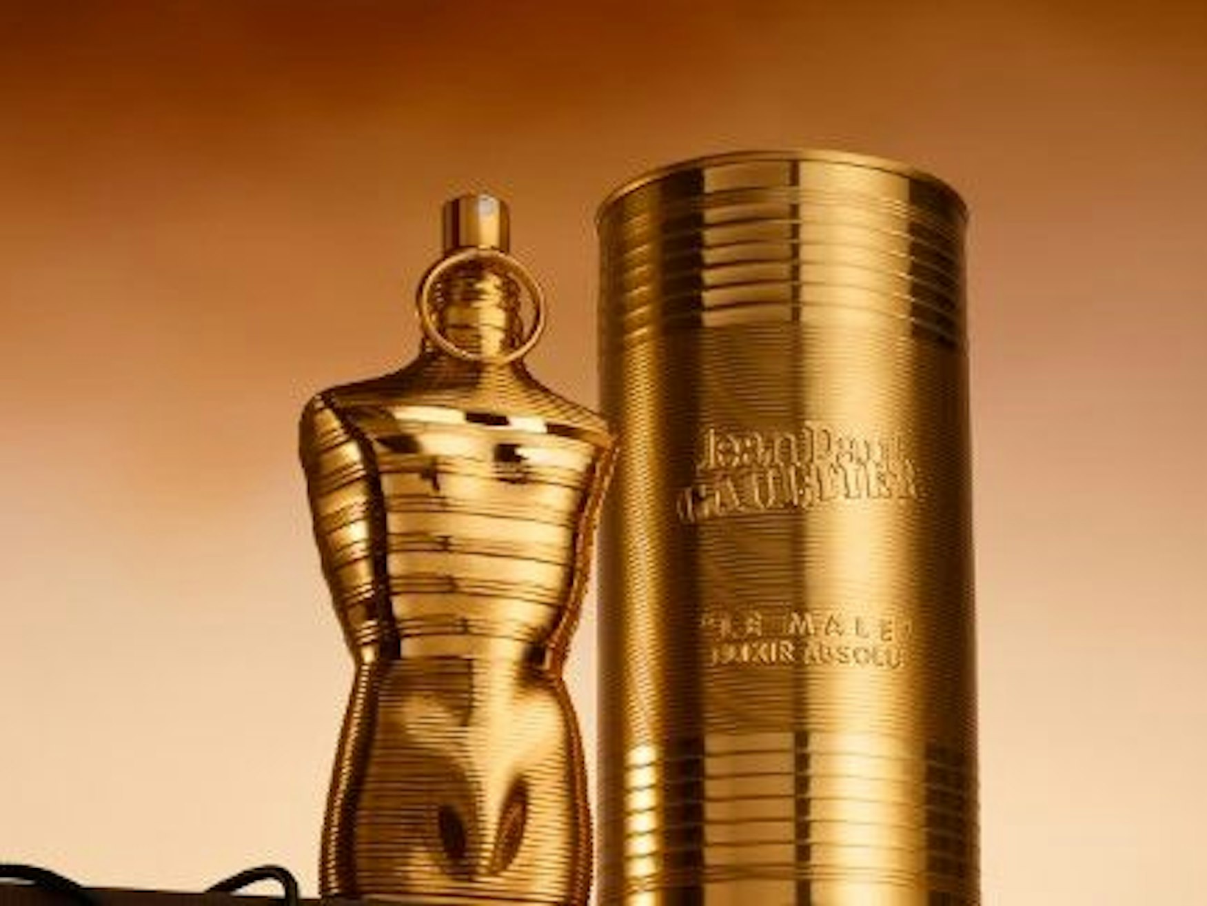 Ein goldener Flakon in Form eines Männertorsos steht neben einer goldenen Dose