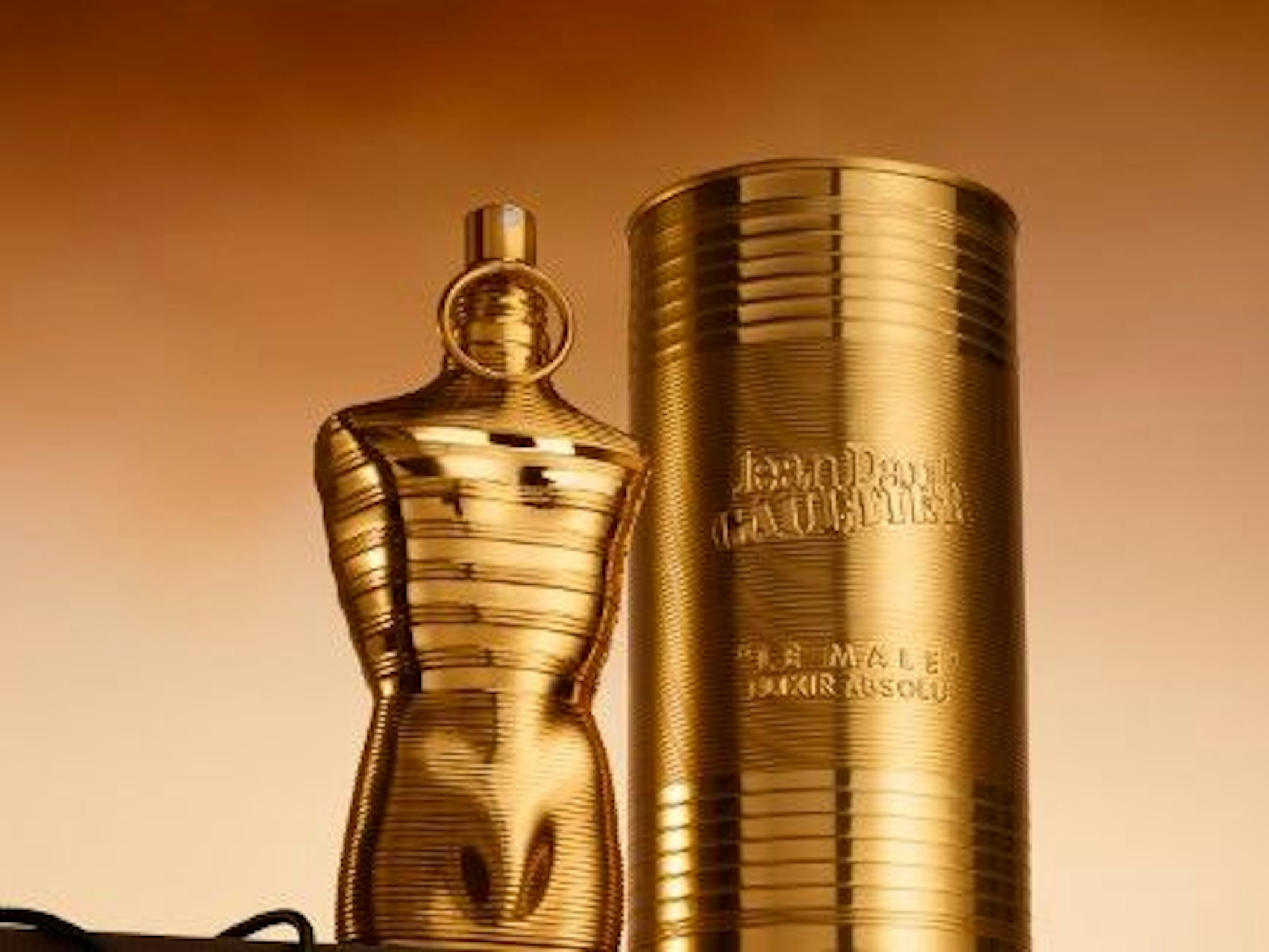 Ein goldener Flakon in Form eines Männertorsos steht neben einer goldenen Dose