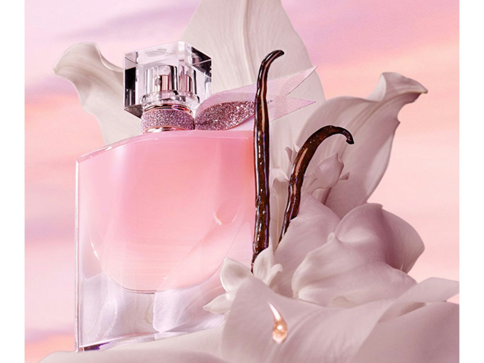 Ein rosa Parfümflakon und zwei Vanilleschoten sind mit Seidenstoff umhüllt