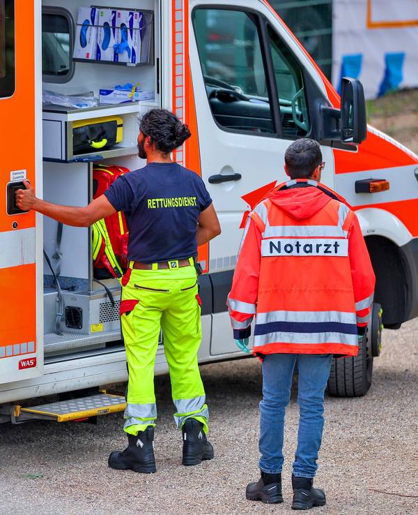 Ein Mitarbeiter des Rettungsdienstes öffnet die Tür eines Rettungswagens, hinter ihm steht ein Mann, der eine Notarzt-Jacke trägt.