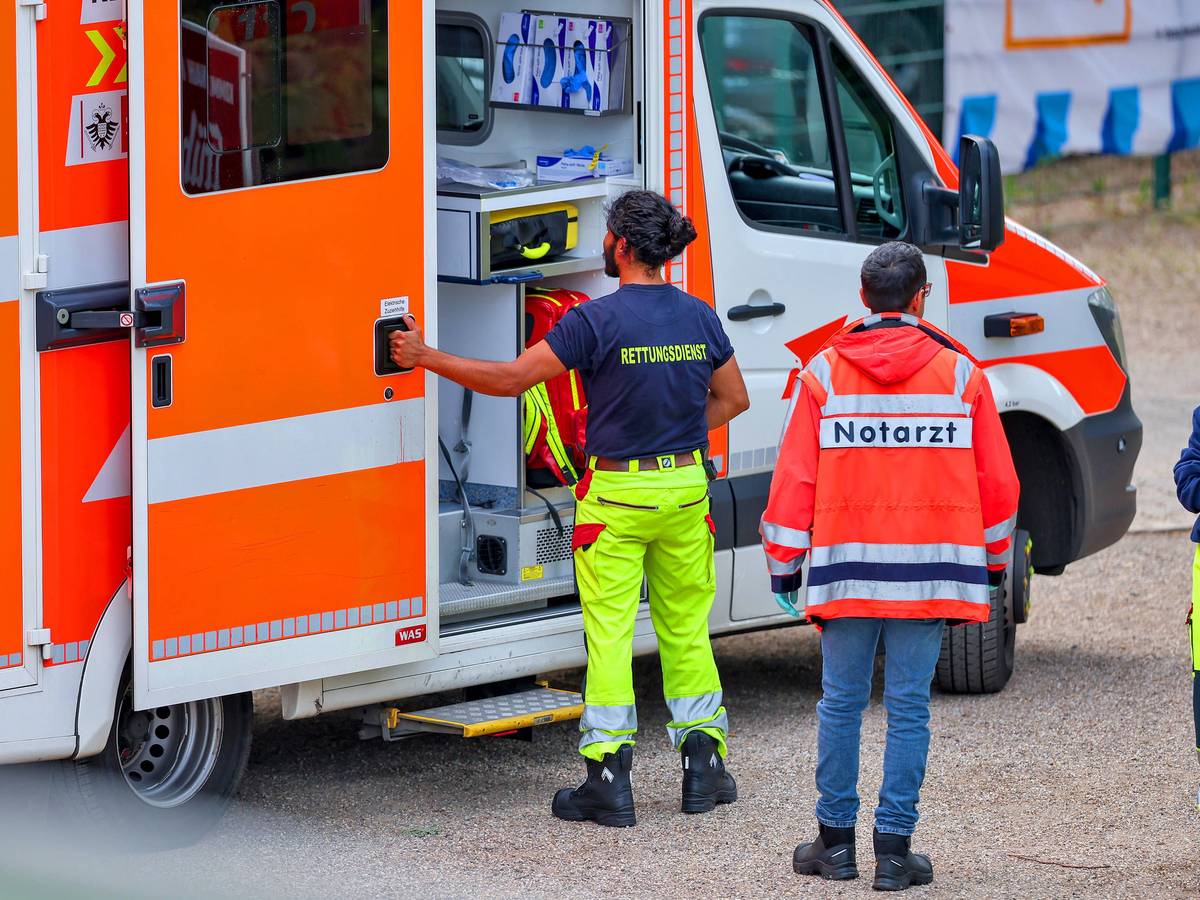Ein Mitarbeiter des Rettungsdienstes öffnet die Tür eines Rettungswagens, hinter ihm steht ein Mann, der eine Notarzt-Jacke trägt.