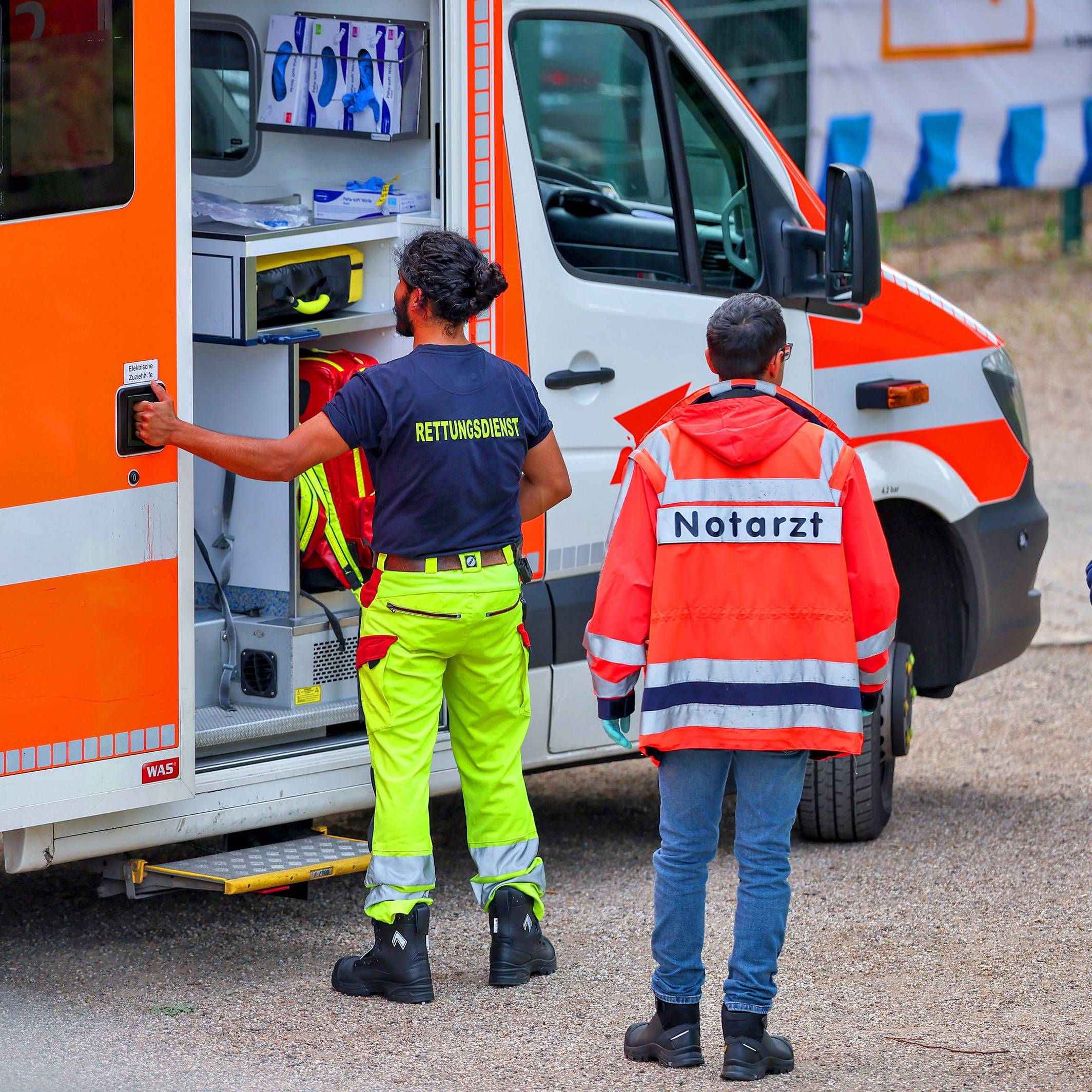 Ein Mitarbeiter des Rettungsdienstes sowie ein Notarzt stehen an einem Rettungswagen.