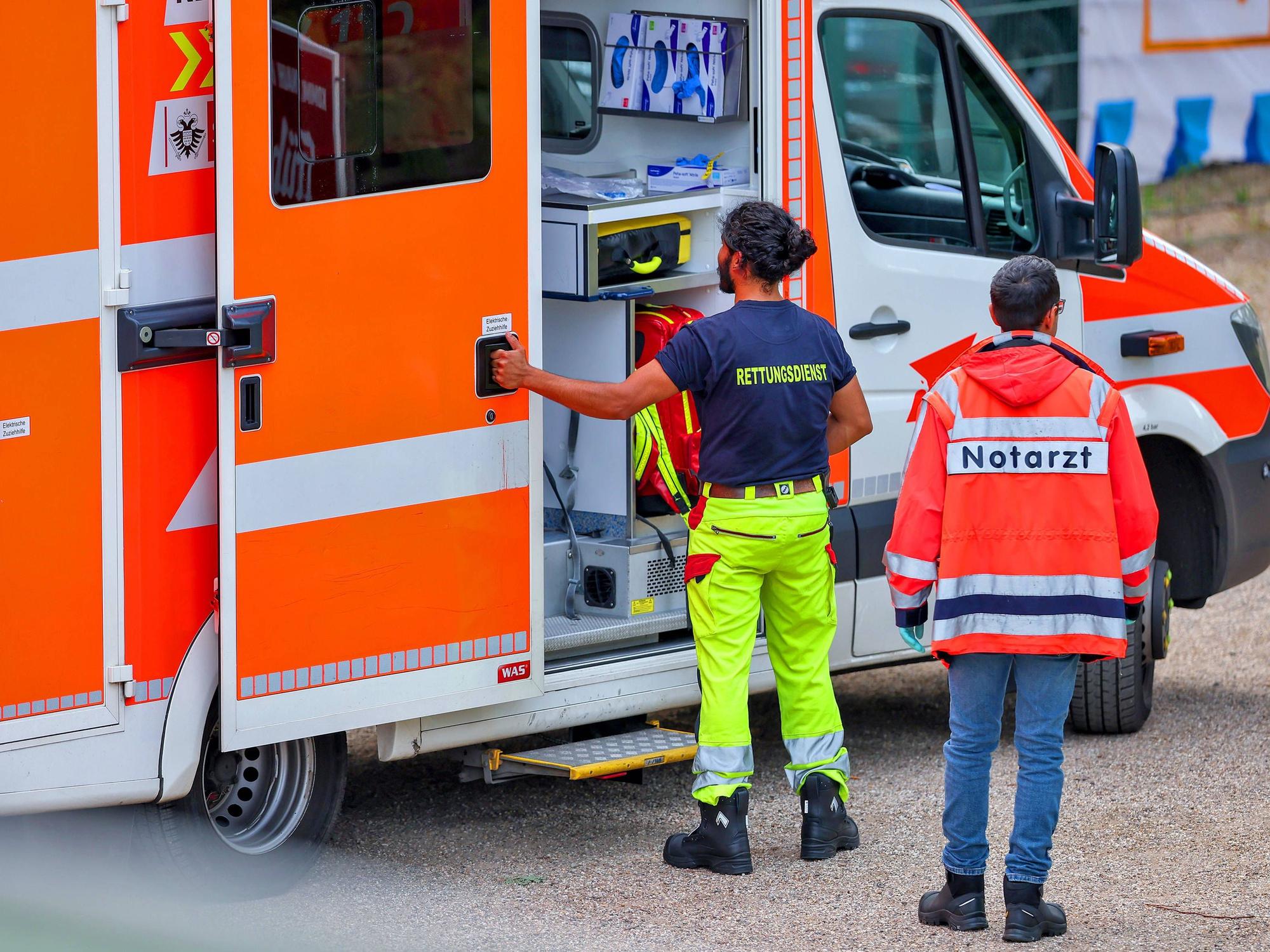 Ein Mitarbeiter des Rettungsdienstes öffnet die Tür eines Rettungswagens, hinter ihm steht ein Mann, der eine Notarzt-Jacke trägt.
