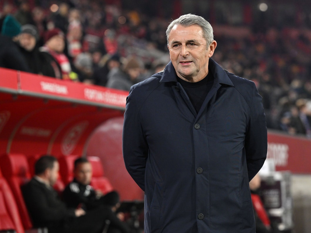 Klaus Allofs hat seine Hände hinter dem Rücken und trägt eine dunkelblaue Jacke.