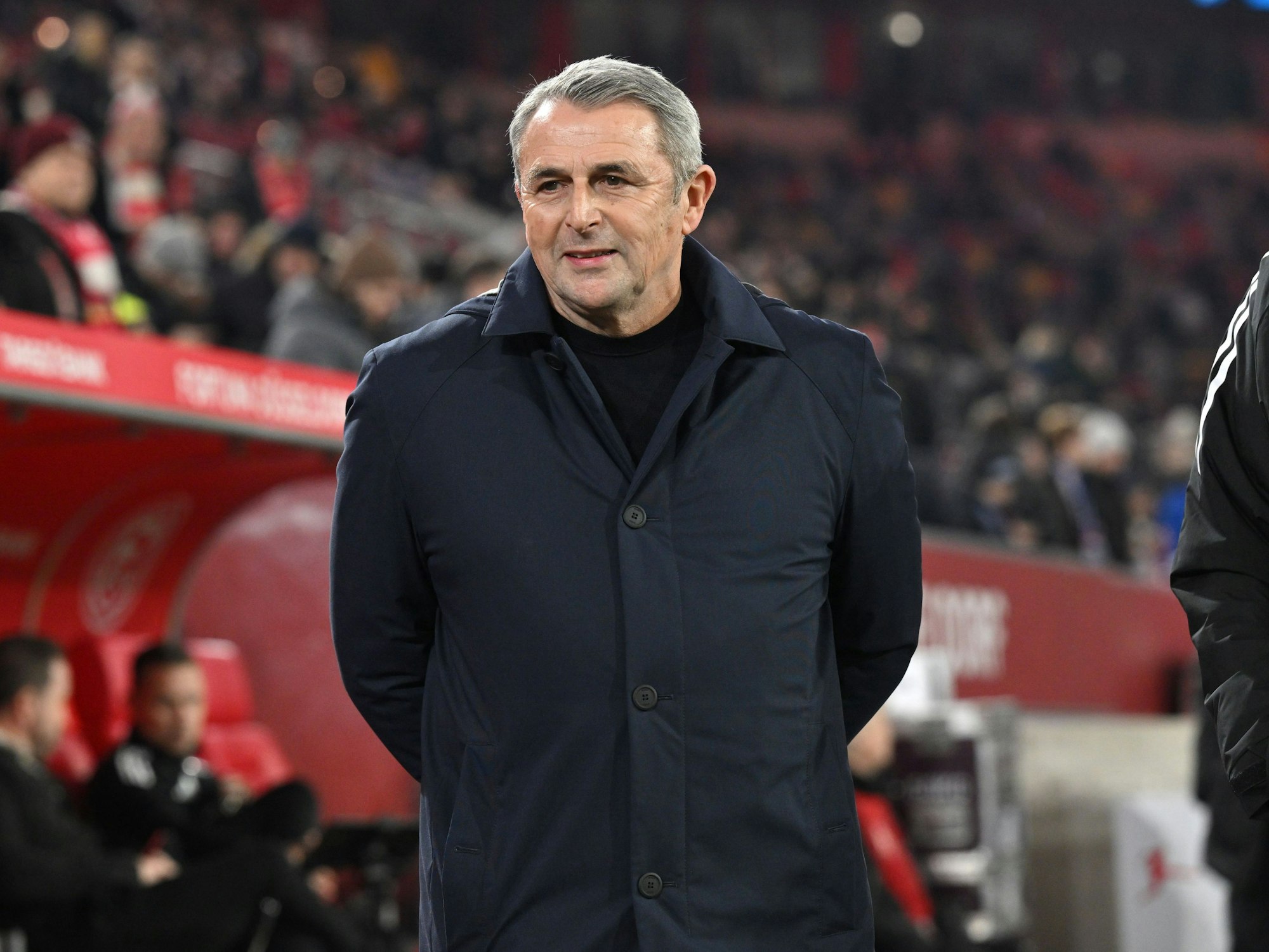 Klaus Allofs hat seine Hände hinter dem Rücken und trägt eine dunkelblaue Jacke.