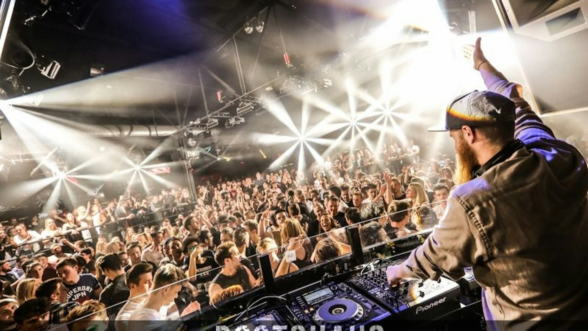 Party People im Bootshaus. Vorne steht der DJ und hält eine Hand in die Höhe.