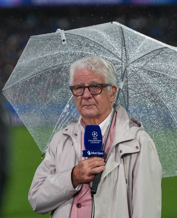 Marcel Reif hat einen durchsichtigen Regenschirm über sich und hält ein blaues Champions-League-Mikrofon in der Hand.