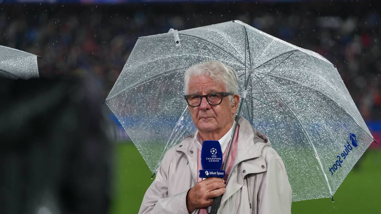 Marcel Reif hat einen durchsichtigen Regenschirm über sich und hält ein blaues Champions-League-Mikrofon in der Hand.