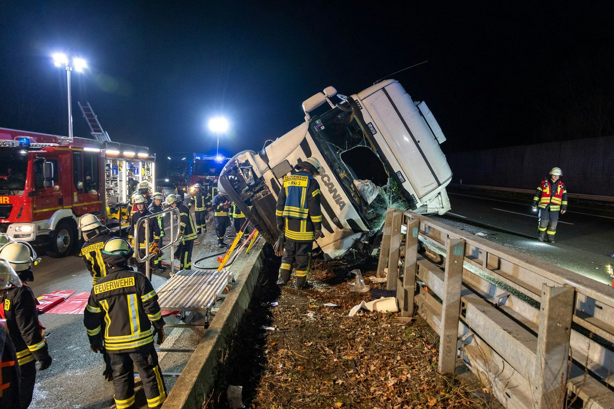 Rettungskräfte sichern die Unfallstelle um das Lkw-Wrack auf dem Mittelstreifen. Auf der A2 zwischen Veltheim und Bad Eilsen ist ein Lkw umgekippt. Laut Polizei schwebt der Fahrer in Lebensgefahr.