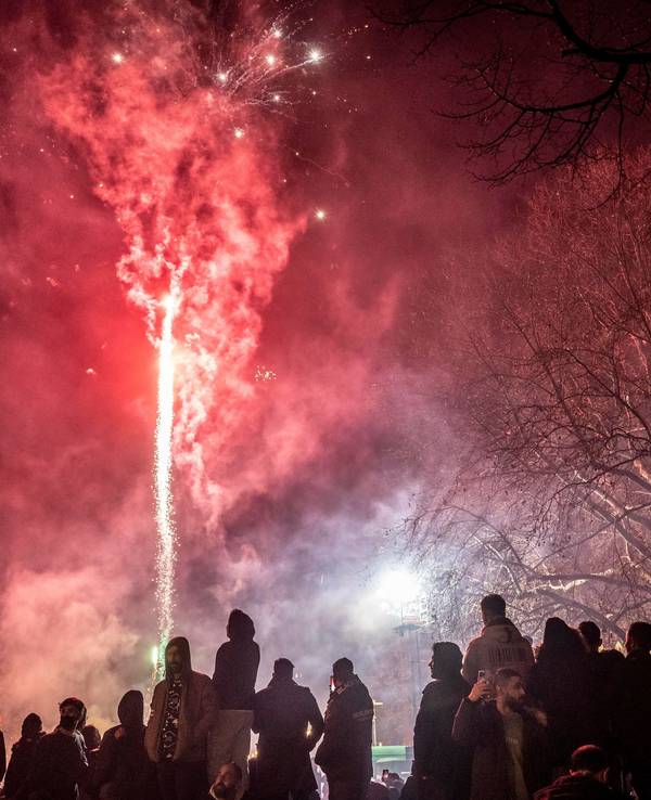 Menschen stehen draußen, vor ihnen schießt eine Silvesterrakete in den Himmel.