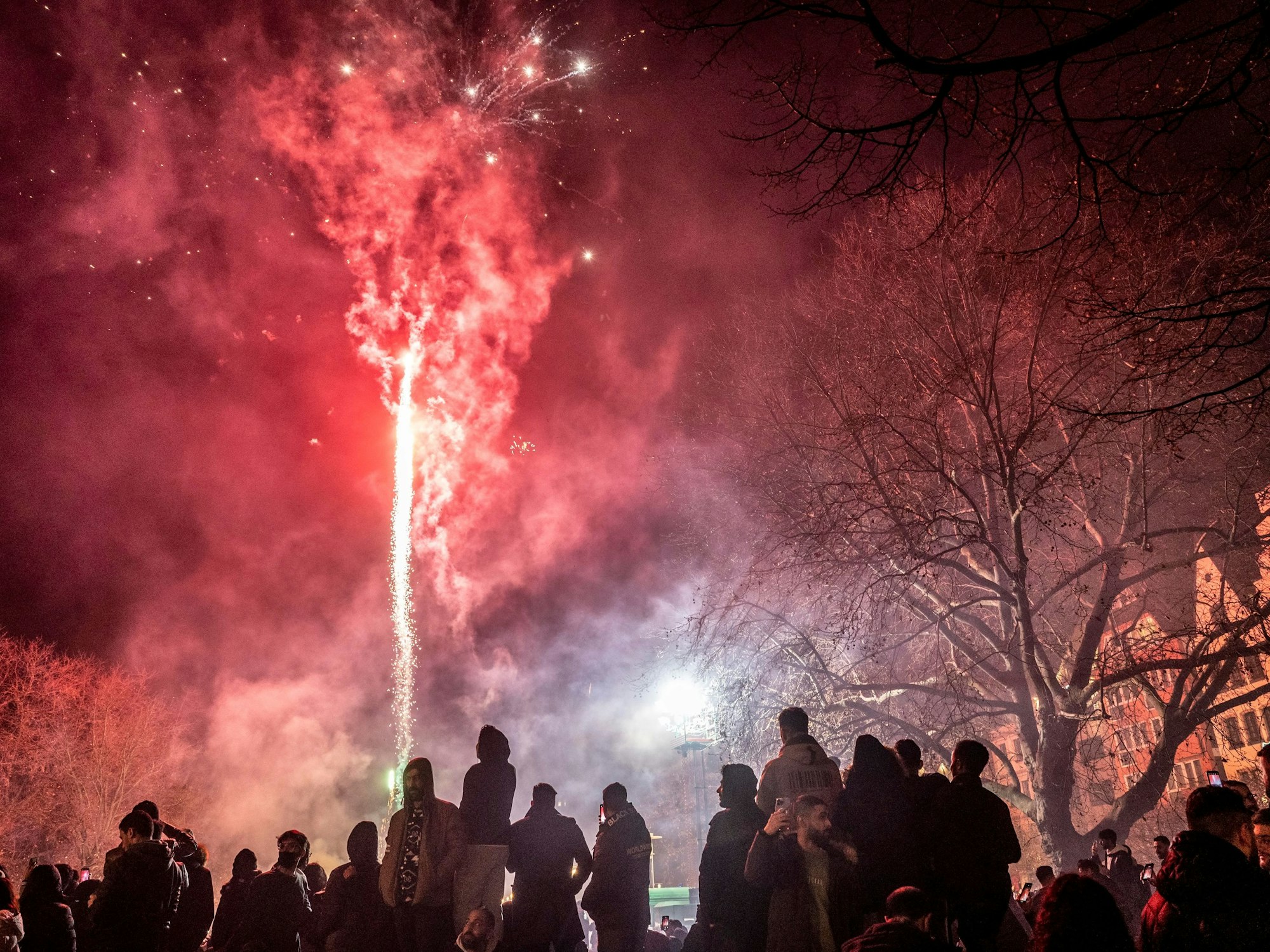 Menschen stehen draußen, vor ihnen schießt eine Silvesterrakete in den Himmel.