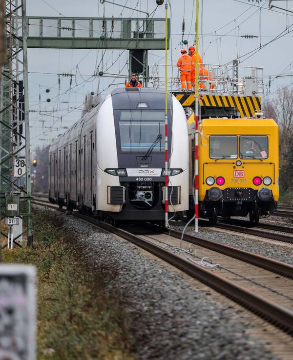 Ein Zug steht auf offener Strecke auf den Gleisen, rechts daneben ein Reparaturzug mit Monteuren, um den Oberleitungsschaden zu beheben.