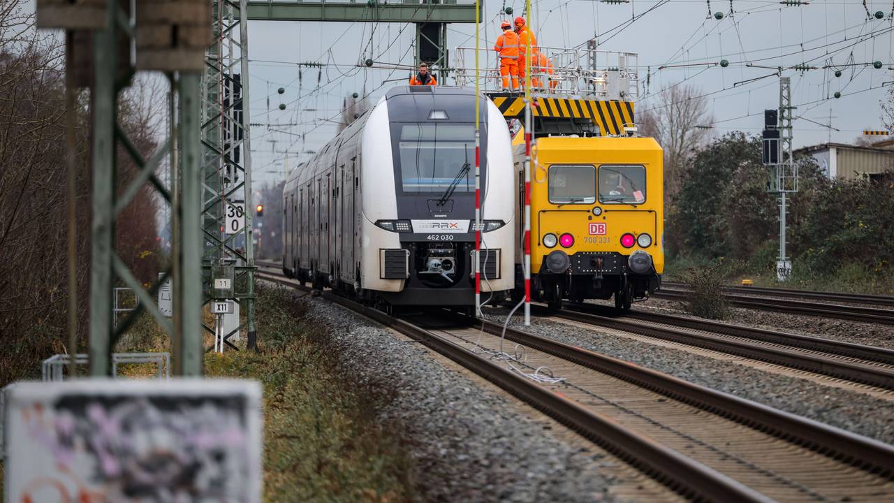 Ein Zug steht auf offener Strecke auf den Gleisen, rechts daneben ein Reparaturzug mit Monteuren, um den Oberleitungsschaden zu beheben.